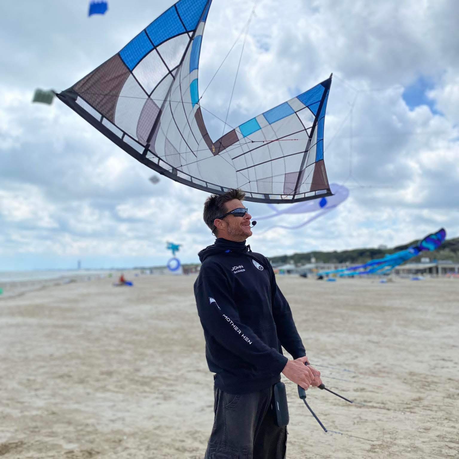 John Barresi holding his kite handles on a beach, looking up at a large kite flying overhead